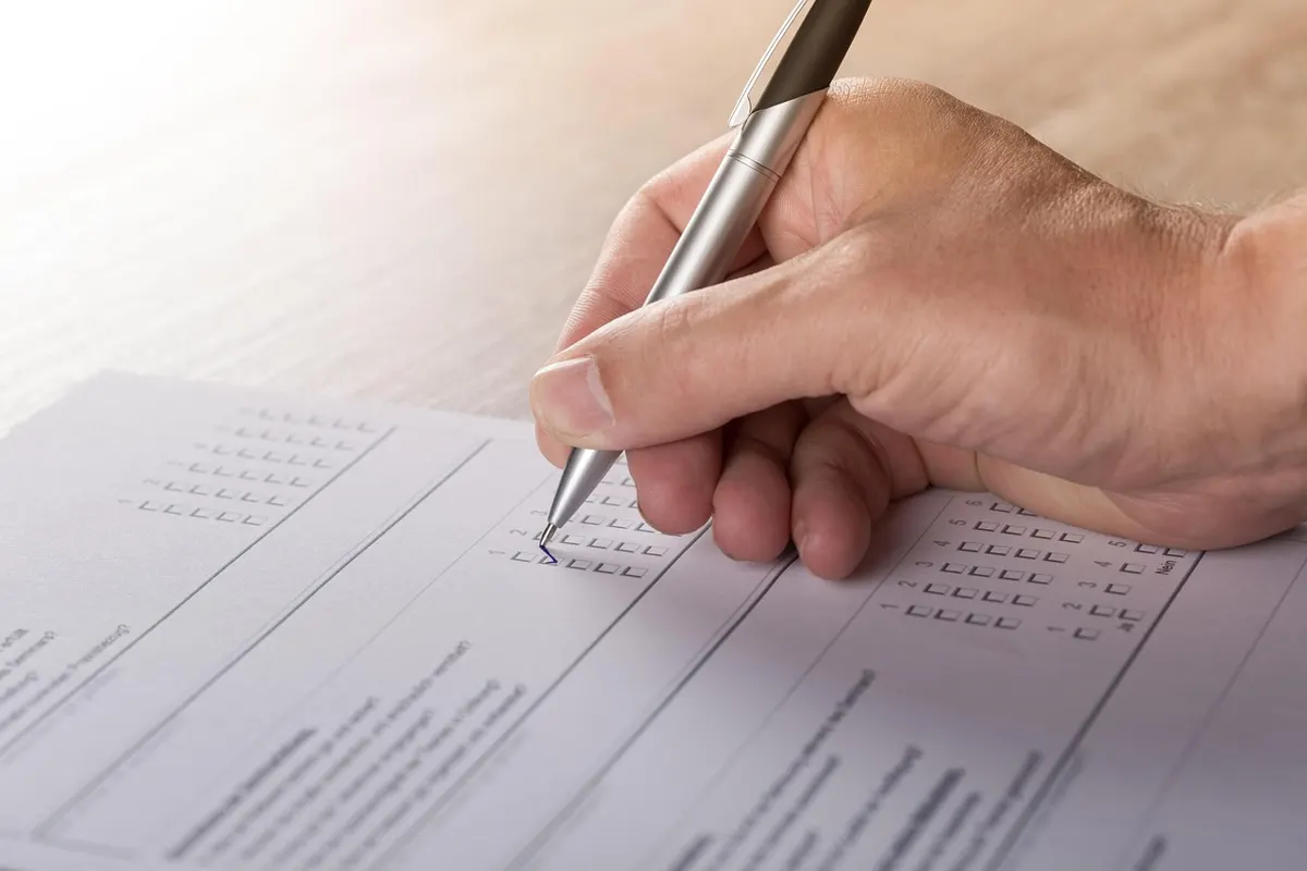 Hand filling checkboxes on a printed personality test form with a pen