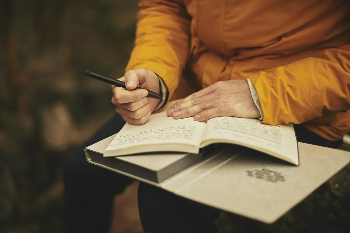 Hands writing in an open notebook with a pen, close-up of person taking notes during reflection