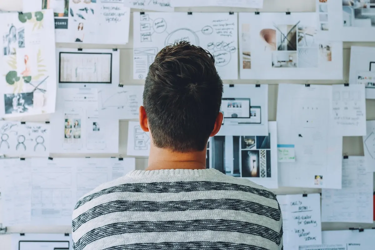 Man seen from behind studying a wall covered with notes, diagrams and personality maps.